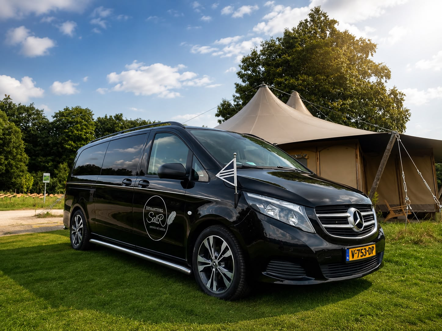 De rouwauto van Uitvaartzorg Sabr op een grasveld bij een ceremonietent